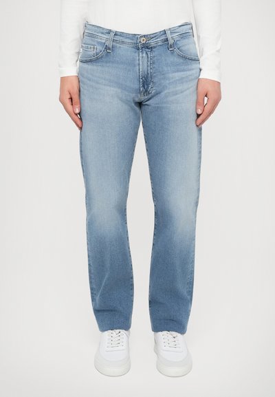 Jean en denim bleu clair avec une coupe droite, avec des poches avant, une fermeture éclair et un léger délavage. Associé à des baskets blanches.