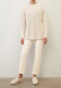 Maglione lavorato a maglia beige con una vestibilità comoda, abbinato a pantaloni dritti di un light beige e scarpe slip-on beige trapuntate.
