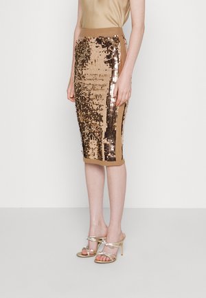 Vrouw draagt een knielange gouden pailletten kokerrok met een hoge taille en metallic gouden sandalen met hoge hakken.