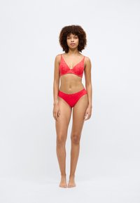 Soutien-gorge en dentelle rouge avec motif floral et décolleté en V, assorti à des culottes brésiliennes en dentelle rouge. Texture lisse, sans éléments métalliques visibles.