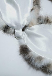 Hvid satin øjenmaske med blødt faux fur kant, der har en glat tekstur og en lille stofsløjfe til justering eller fastgørelse.