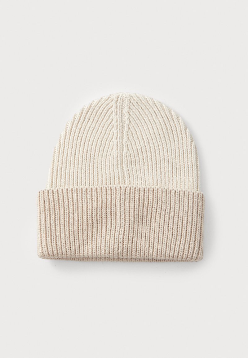 Bonnet en tricot de couleur crème clair et beige, présentant une texture côtelée et un revers replié. Design simple, sans motifs ni embellissements.