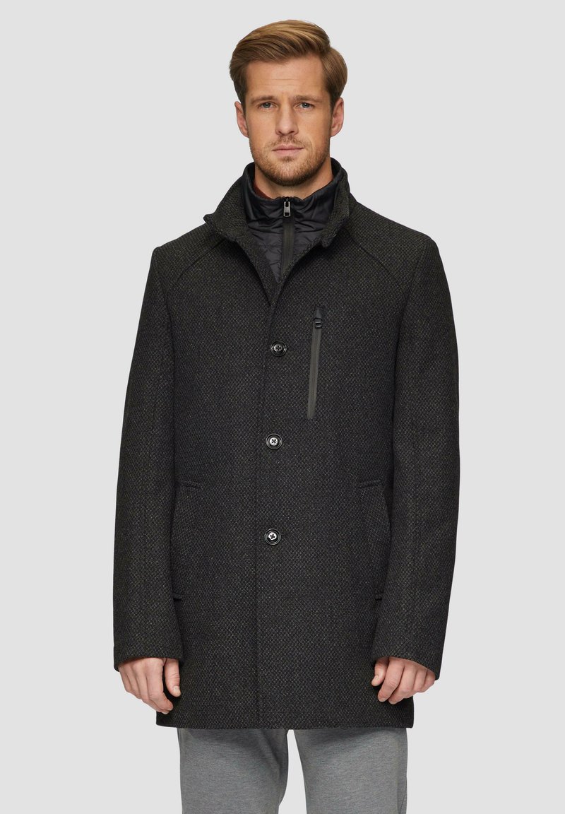 Donkergrijze jas met een gestructureerde afwerking, voorzien van een hoge kraag, knoopsluiting en een ritszak op de borst voor extra functionaliteit.