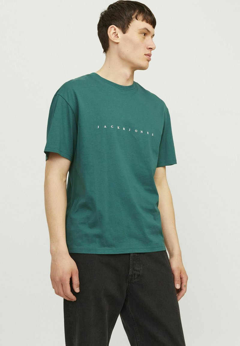 Grünes Baumwoll-T-Shirt mit kurzen Ärmeln, Rundhalsausschnitt und weißem, zentral auf der Vorderseite platziertem "JACK & JONES"-Text. Einfache, glatte Textur.