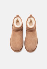 Ζευγάρι μπότες χειμερινές από καφέ σουέντ με λευκή αφράτη επένδυση, φωτογραφημένες από πάνω σε λευκό φόντο.