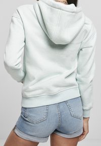 Felpa verde menta con finitura testurizzata, caratterizzata da un ampio cappuccio e polsini a coste, abbinata a pantaloni jeans corti arrotolati.