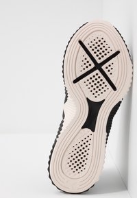 Zwarte schoenenzool met een textuur van witte rubber, voorzien van een kruispatroon en meerdere perforaties voor grip en flexibiliteit.