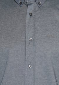 Grau button-down Hemd aus strukturiertem Stoff, mit einem spitzen Kragen, sechs Knöpfen und einem kleinen Logo auf der linken Seite.