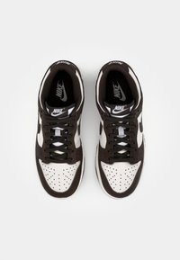 Nike tenisky s bílým a hnědým koženým svrškem, perforovanou špičkou, černými tkaničkami a logem na jazyku a na boku.