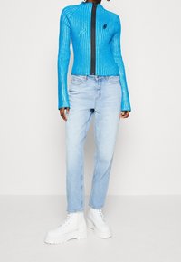 Blå ribbad stickad zip-jacka med långa ärmar, i kombination med ljusblå denimjeans och vita kraftiga snörstövlar.