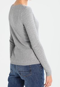 Szary sweter z dzianiny prążkowanej, z długimi rękawami, zaokrąglonym dekoltem i dopasowanym krojem, zestawiony z jeansami, prezentujący fakturowaną tkaninę.