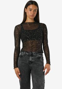 Črna prozorna majica z dolgimi rokavi in z zlatimi pikami; kvadratni izrez; v kompletu s hlačami iz sivo-jeans tkanine z visokim pasom. Gladka tekstura.