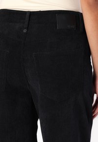 Czarne spodnie z korduru o pionowej teksturze prążkowanej. Posiadają dwie tylne kieszenie oraz prostą skórzaną naszywkę w pasie.