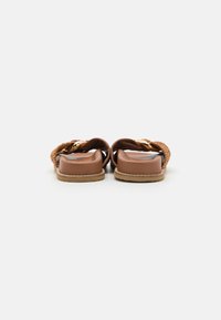 Brown sandals with woven detailing and a smooth leather finish. Features a flat sole and gold buckle accents for closure.