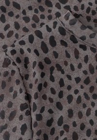Gros plan d’un tissu gris avec des taches noires irrégulières dans un motif léopard, montrant une texture et des coutures détaillées.