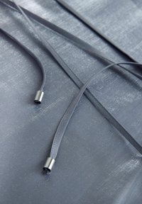 Szürke szaténanyag enyhe fényességgel, sima szalagokkal ezüst fémvégződésekkel és dombornyomott mintával a felületen.