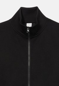 Sort zip-jakke med høj krave, lavet af blødt materiale. Har en sølv lynlås og subtile syningen detaljer.