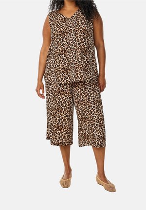 Frau trägt ärmelloses Oberteil mit Leopardenmuster und passende, weit geschnittene, gekürzte Hose mit beigefarbenen gewebten Ballerinas vor weißem Hintergrund.