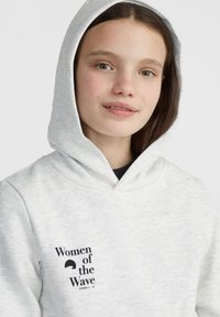 Sudadera gris claro con un bolsillo frontal y un estampado gráfico negro que dice "Mujeres de la Ola". Presenta un capucho con cordón y una textura suave.