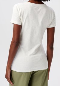 Camiseta ajustada de manga corta en color crema claro con detalles moteados en azul, hecha de tela suave. Presenta un escote redondeado y puños enrollados.