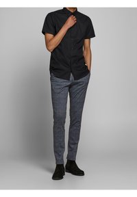 Svart kortärmad skjorta med knappar i kombination med grårutiga skräddarsydda byxor och svarta mockastövlar. Slät tygkvalitet och slim fit-design.