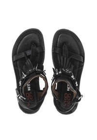 Un par de sandalias de cuero negro con flecos y tachuelas metálicas, correas alrededor del tobillo y detalles impresos en la suela, vistas desde arriba sobre un fondo blanco.