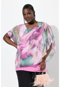 Top floreale con tessuto fluido e trasparente in tonalità di rosa e verde. Design sovrapposto con una base rosa solida; accessorato con una borsa rosa frangiata.