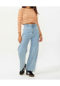 Stribet orange cropped sweater med lange Ærmer, parret med høj talje lys blå brede bukser og sorte sneakers med hvide striber.