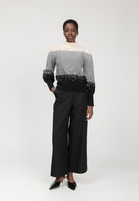 Maglione grigio a ombre con design a trecce e accenti luccicanti, con alto collo, abbinato a pantaloni neri a gamba larga e tacchi.