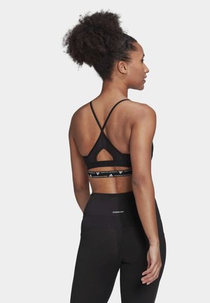 Sujetador deportivo negro con tirantes ajustables, detalle recortado en la parte posterior y banda elástica con logo. Combinado con leggings negros de cintura alta.