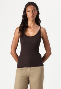 Débardeur marron à fines bretelles, design ajusté et texture lisse, associé à un pantalon beige. Style simple et polyvalent.