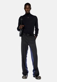 Maglione nero a collo alto, slim fit; pantaloni sartoriali con pannelli laterali blu scuro; accessor preso con una cintura nera e una borsa a spalla.