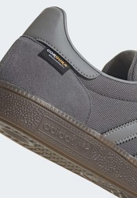 Gray sneaker featuring a suede upper, textured mesh, CorDurabrand tag, and patterned rubber sole with an embossed logo.
