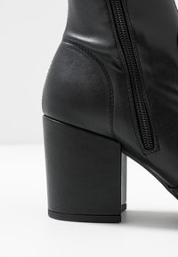 Black leather ankle boot featuring a block heel, zip closure, smooth texture, and sleek design.