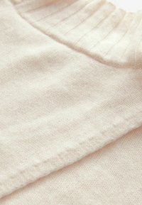 Suéter de punto color beige claro con cuello de canalé y textura suave, con un patrón de tela liso y uniforme, sin adornos visibles.