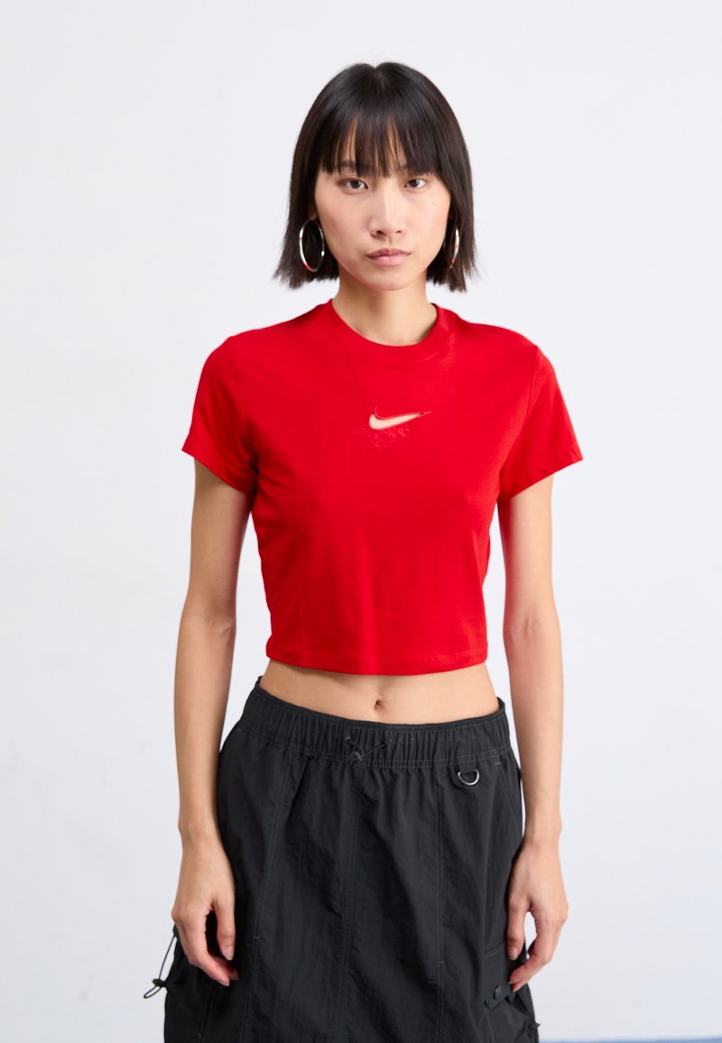 Czerwona, skrócona koszulka z bawełny z małym, białym logo Nike na piersi. W połączeniu z czarną spódnicą z elastycznym paskiem i sznurkiem.