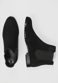 Schwarze Wildleder-Ankle Boots mit elastischen seitlichen Einsätzen, runder Zehenpartie und einer glatten schwarzen Gummisohle, die ein minimalistisches Design aufweisen.