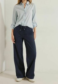 Ljusblårandig skjorta med knappar och uppvikta ärmar i kombination med marinblå vida byxor med dragsko i midjan, bärs med vita sneakers.