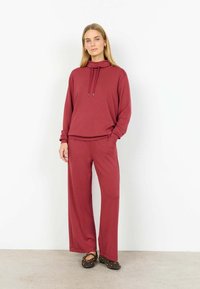 Trusă de lounge maro-vișinie, formată dintr-un hanorac cu glugă și șnururi și pantaloni lejeri. Material neted cu o siluetă relaxată.