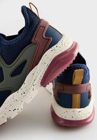 Baskets en maille bleu marine avec des accents verts et bordeaux, semelle en caoutchouc avec des détails blanc moucheté et onglet de talon texturé.