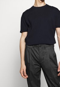Marinblå bomulls-T-shirt med kort ärm, i kombination med grå skräddarsydda byxor med knappstängning och sidofickor.