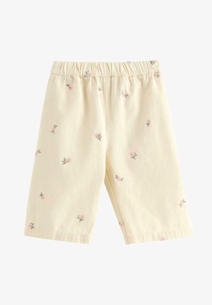 Kermanväriset pikkulasten shortsit, joissa pienet vaaleanpunaiset kukkakuviot ja joustava vyötärönauha, valmistettu pehmeästä kankaasta.