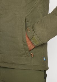 Groene outdoorjas met een zip pocket, klittenbandmanchetten en leren accenten. Inclusief een blauw en gele Zweedse vlag detail.