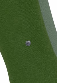 Zwei Paar Socken sind ausgestellt. Das eine Paar ist dunkelgrün mit einem silbernen Logo, das andere hellgrün, was einen komplementären Farbkontrast schafft.