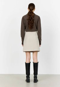 Brun stickad tröja med långa ärmar, kombinerad med en texturerad beige minikjol och svarta knähöga stövlar.