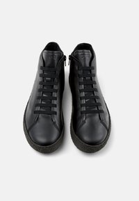 Zapatos negros de caña alta hechos de cuero con suelas de goma texturizadas, con cordones planos y una cremallera lateral. Logo de la marca en la lengüeta.