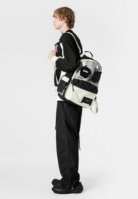 La mochila presenta una combinación de tela negra y gris claro, detalles reflectantes, múltiples compartimentos y correas acolchadas para mayor comodidad.