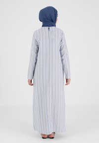 Robe longue rayée bleue et blanche, en tissu léger, avec des manches longues, un col arrondi et un détail de bouton au dos.