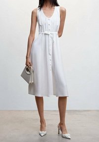 Valkoinen, hihaton mekko napituksella edessä ja vyötäröllä vyö. Sujuva kangas, polvipituinen, yhdistetty vaaleanharmaaseen käsilaukkuun ja valkoisiin korkokenkiin.