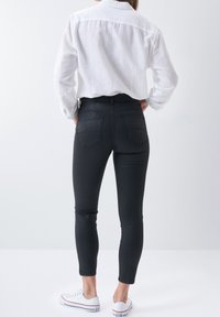 Black jeans with a fitted design, featuring back pockets and minimal stitching, paired with a white long-sleeve shirt and white sneakers.